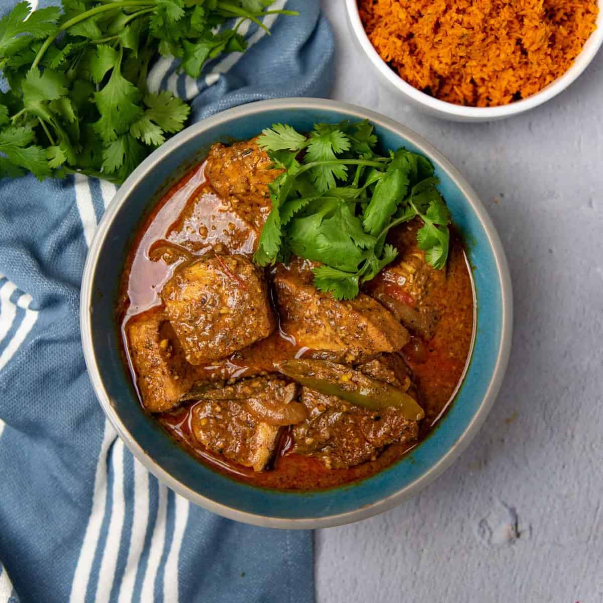 A bowl of spiced fish curry with a rich, red gravy.